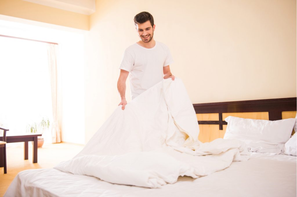 Man making his bed after waking up in the morning.