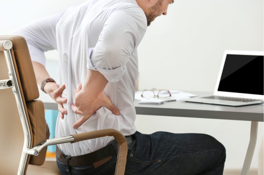 A man experiencing back pain while working in the office.