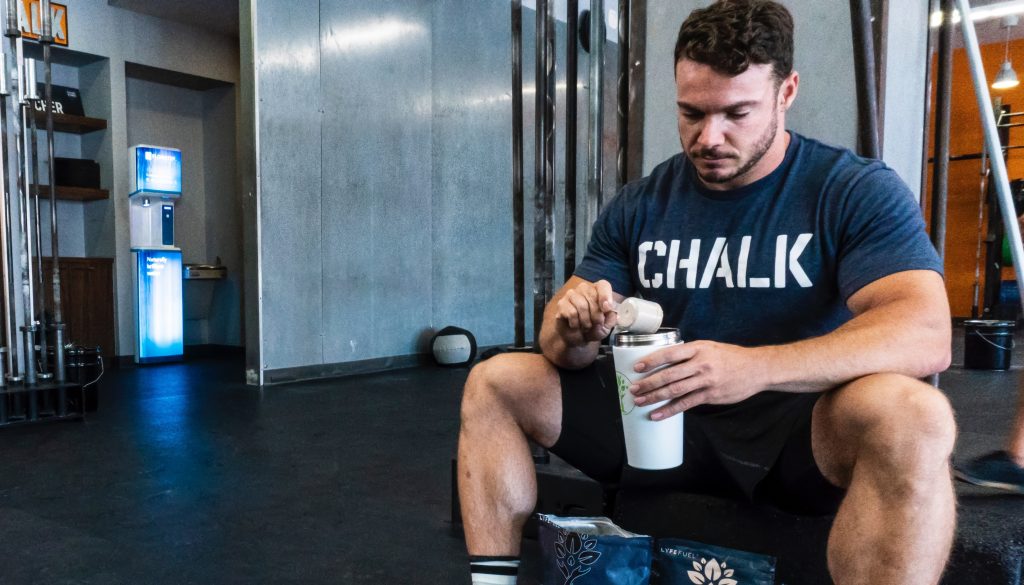 A man putting protein powder on his shaker bottle thinking how much protein he needs daily.