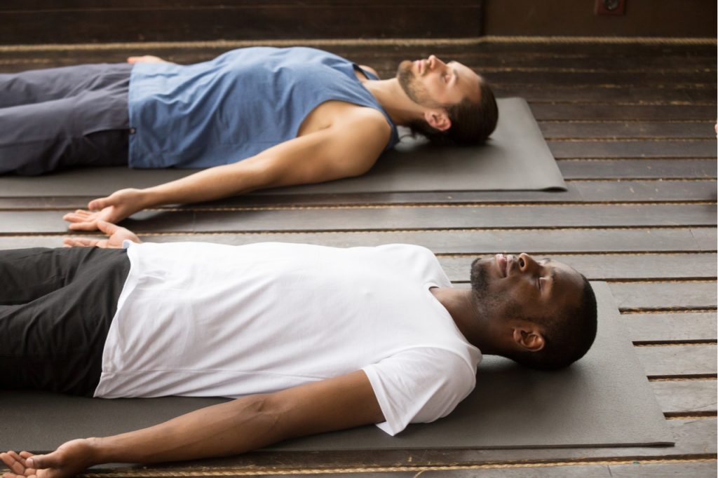 Two men doing the restorative savasana pose.