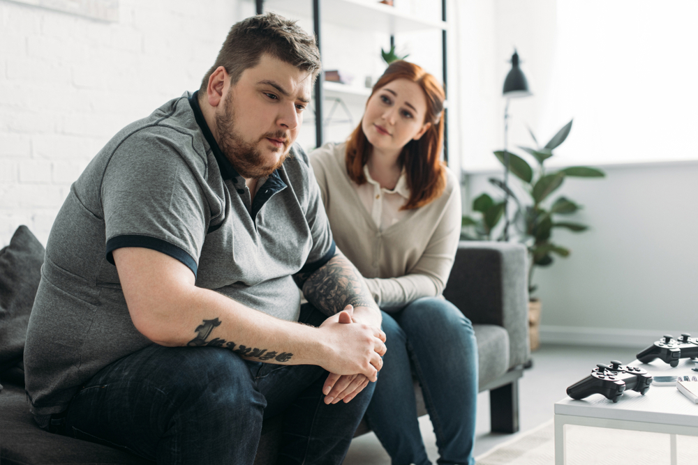 An obese man looking sad while sitting with his girlfriend.