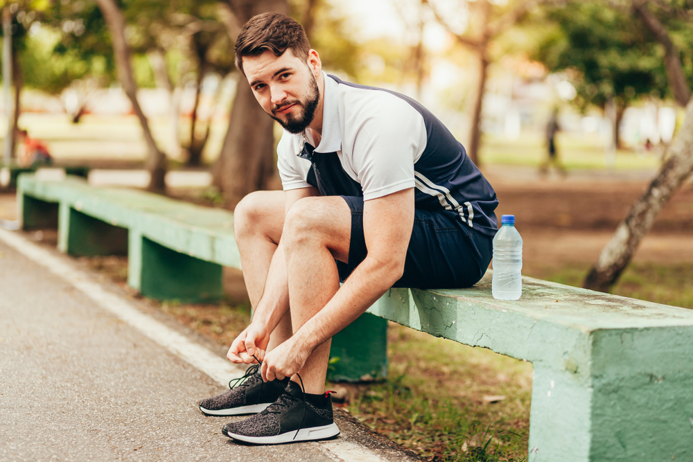 Man sitting on a bench while tying his shoe lace.