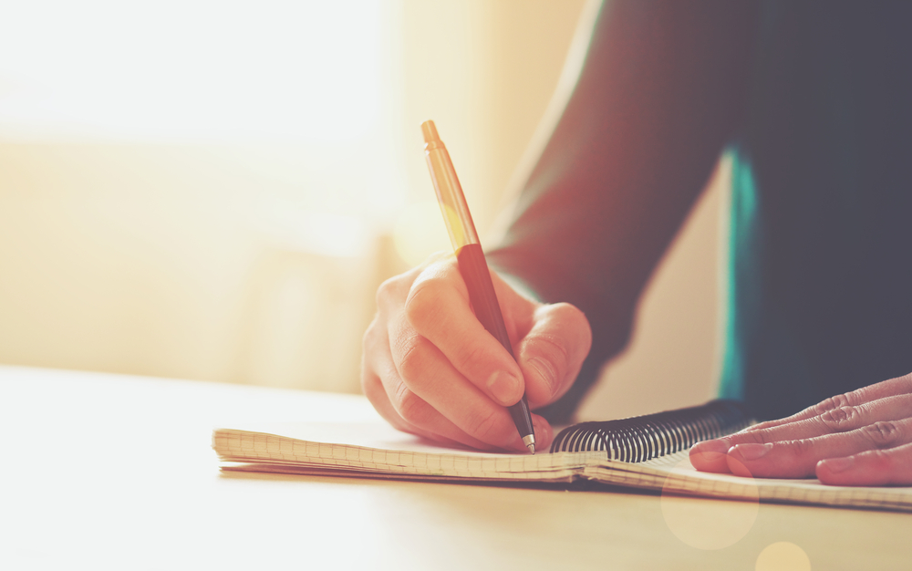 A woman writing on her notebook on how to budget for a trip.