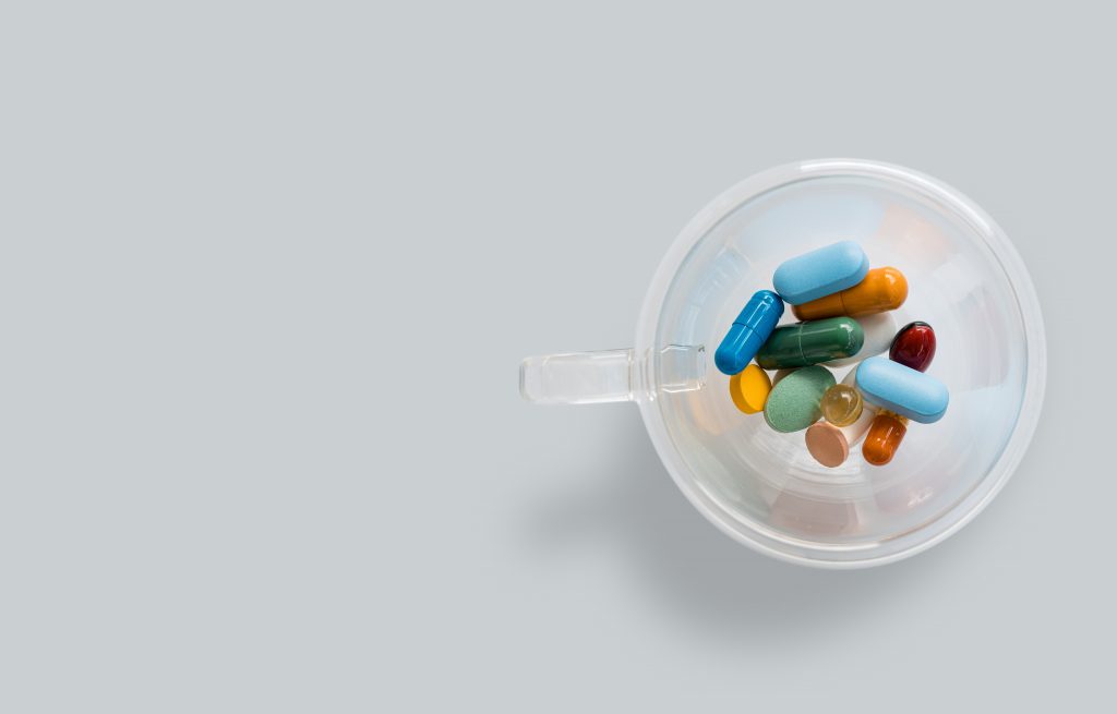 Taking supplements in tablet and capsule type in a cup with white background.