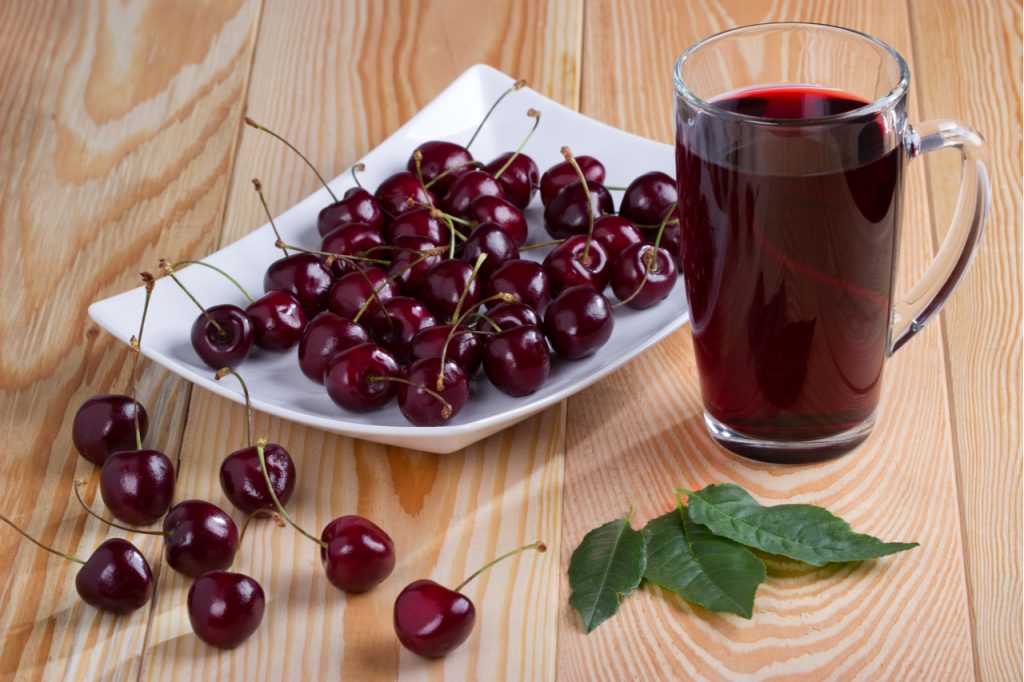 A plate of tart cherry next to a glass of its fresh juice.