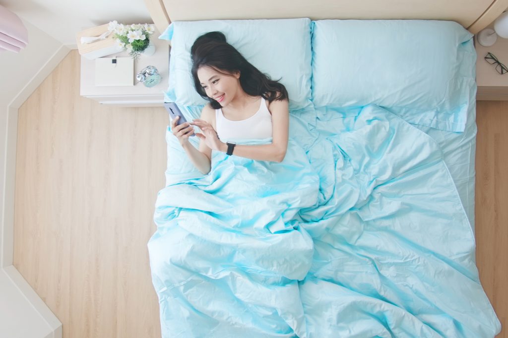 Woman using cellphone while in bed, looking like sending text messages.
