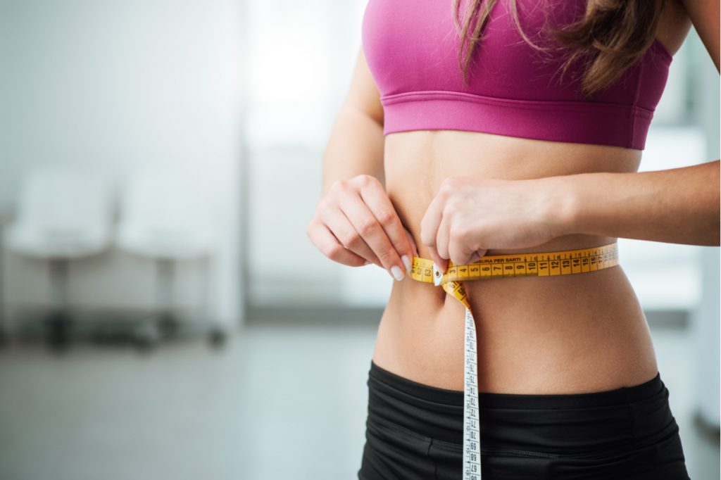 A woman measuring her waist using a tape measure.