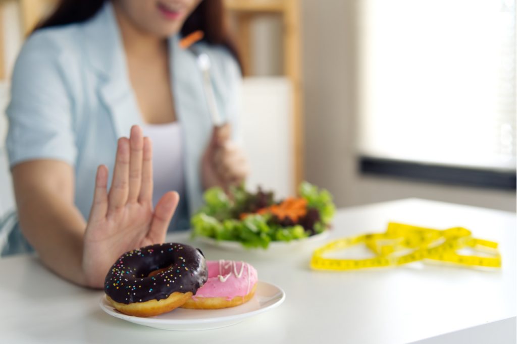 Woman rejecting donuts to eat a salad. Which shows that she is avoiding sugar.