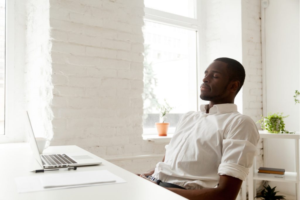 Man relaxing after work breathing fresh air sitting at home office desk with laptop.
