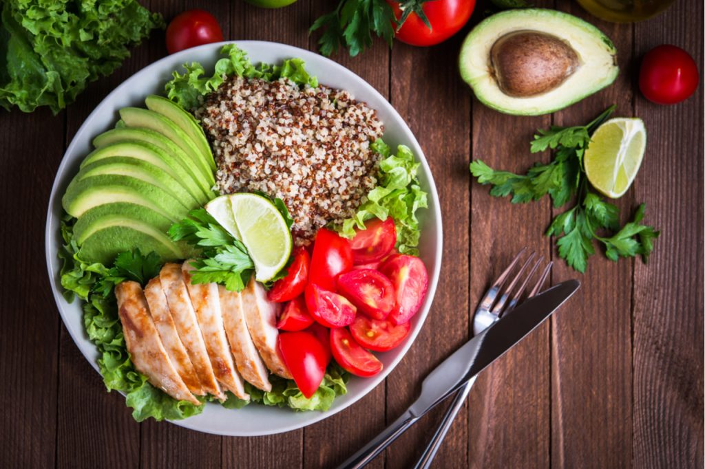 Healthy salad bowl with quinoa, tomatoes, chicken, avocado, lime and mixed greens, lettuce, parsley on wooden background top view
