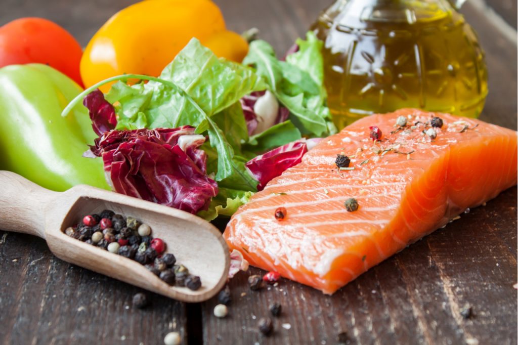 A slice of fresh salmon with vegetables on a wooden table.