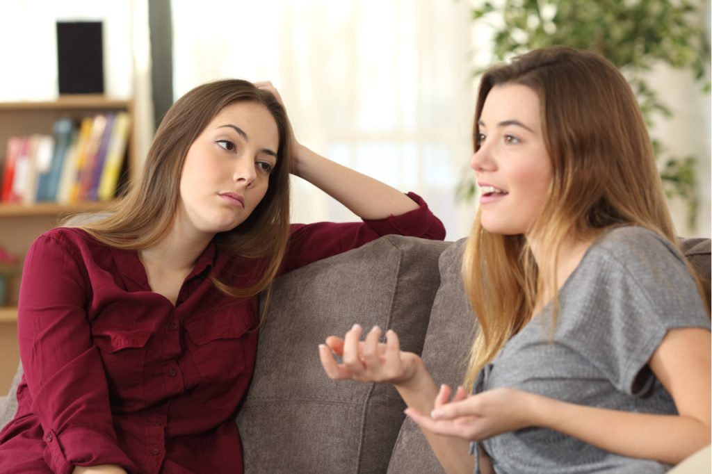 Girl listening to her friend having a conversation sitting on a couch in the living room at home