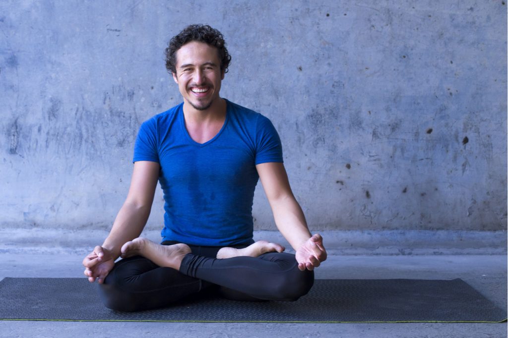 A man smiling happily while doing yoga.