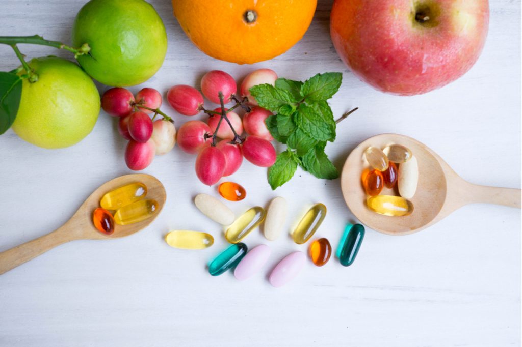 Multivitamin supplements from fruit on white wood background with wooden spoon.