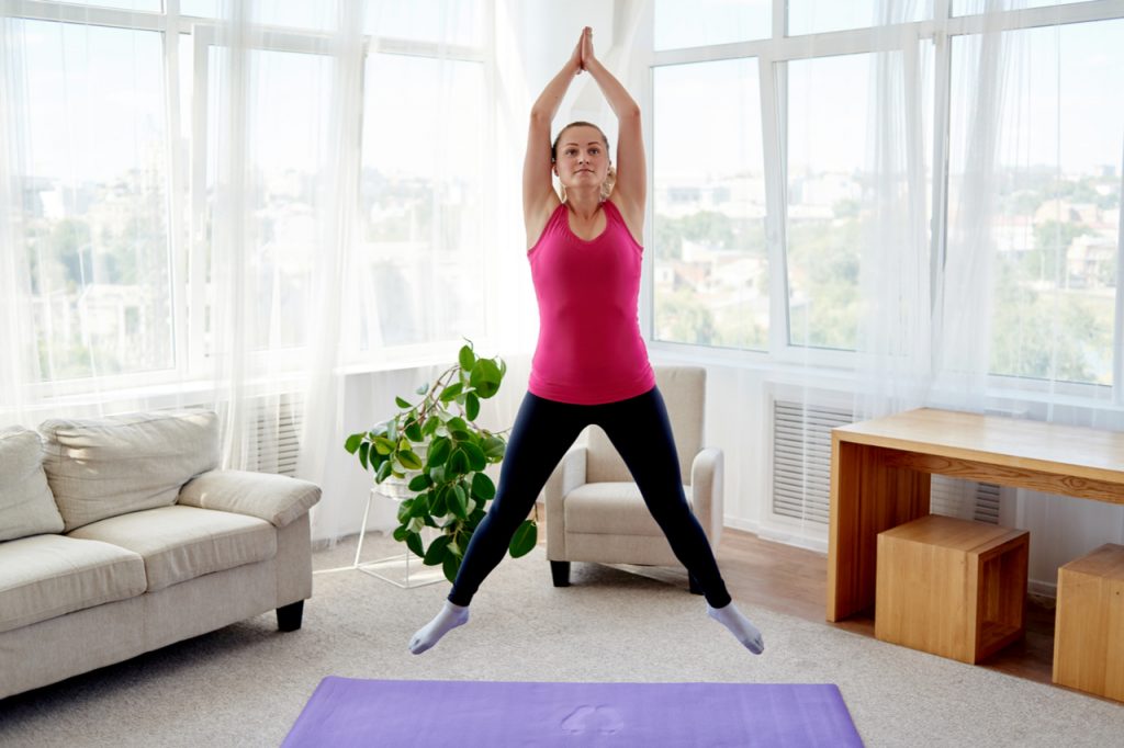 A woman doing jumping jacks in her living room.