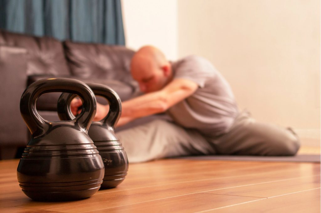 A man doing workout in his living room next to his kettlebell.