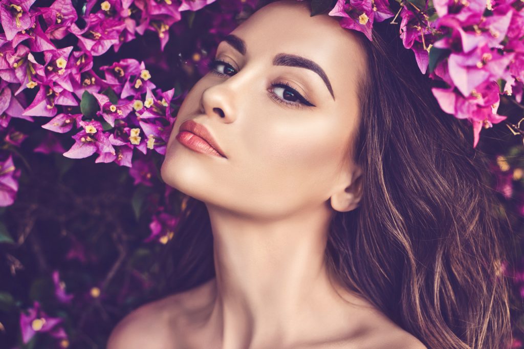 A woman posing for spring makeup with flowers on the background.