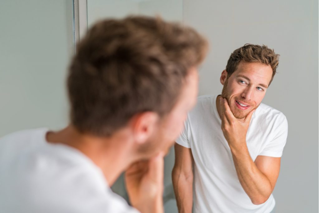 Man looking at the mirror, feeling good about himself being clean.