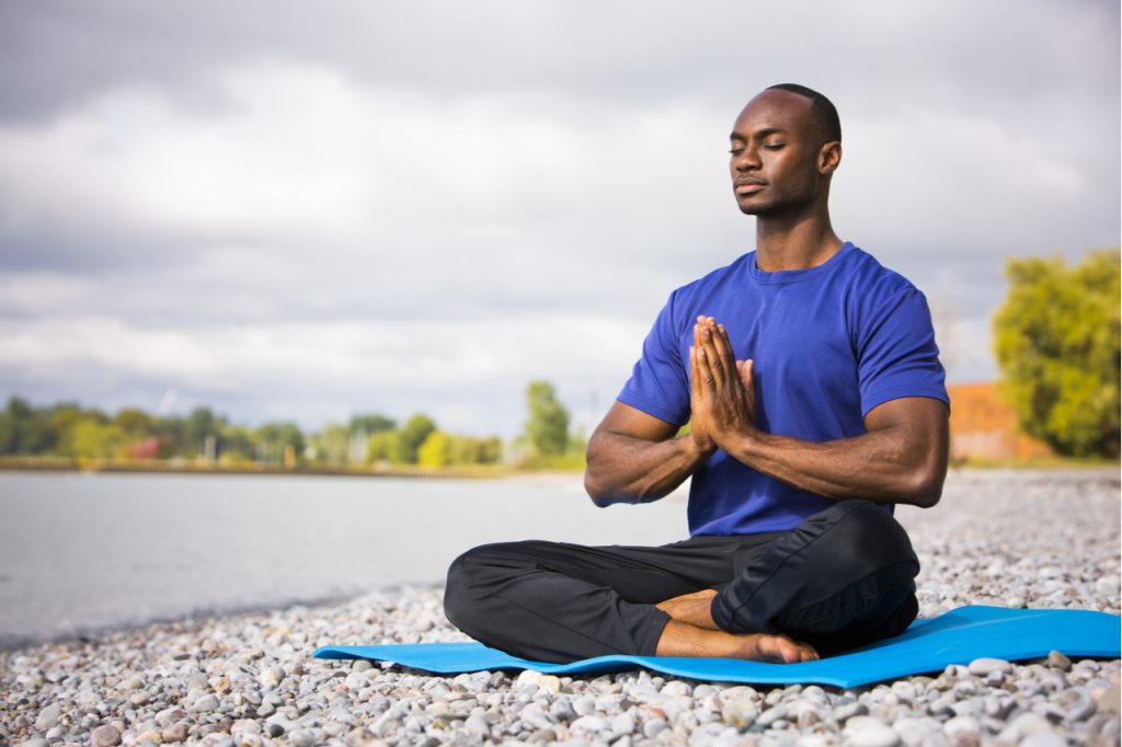 A man wearing athletic wear sitting on the beach exercising yoga