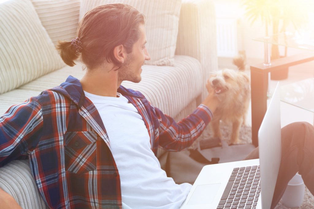 Man stroking his pet and working on laptop as pet therapy.