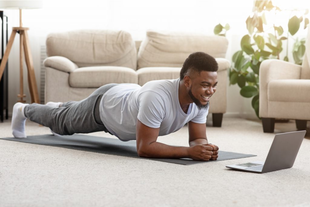 A man enjoying his plank workout while looking at his laptop