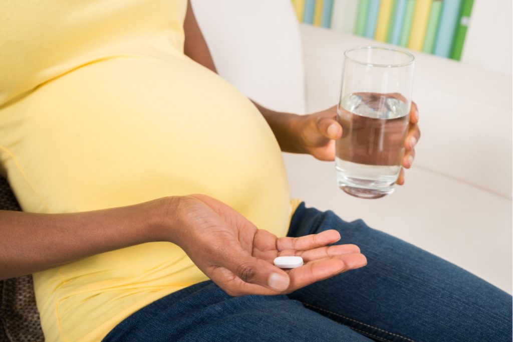 A pregnant woman holding a vitamin pill and glass of water.