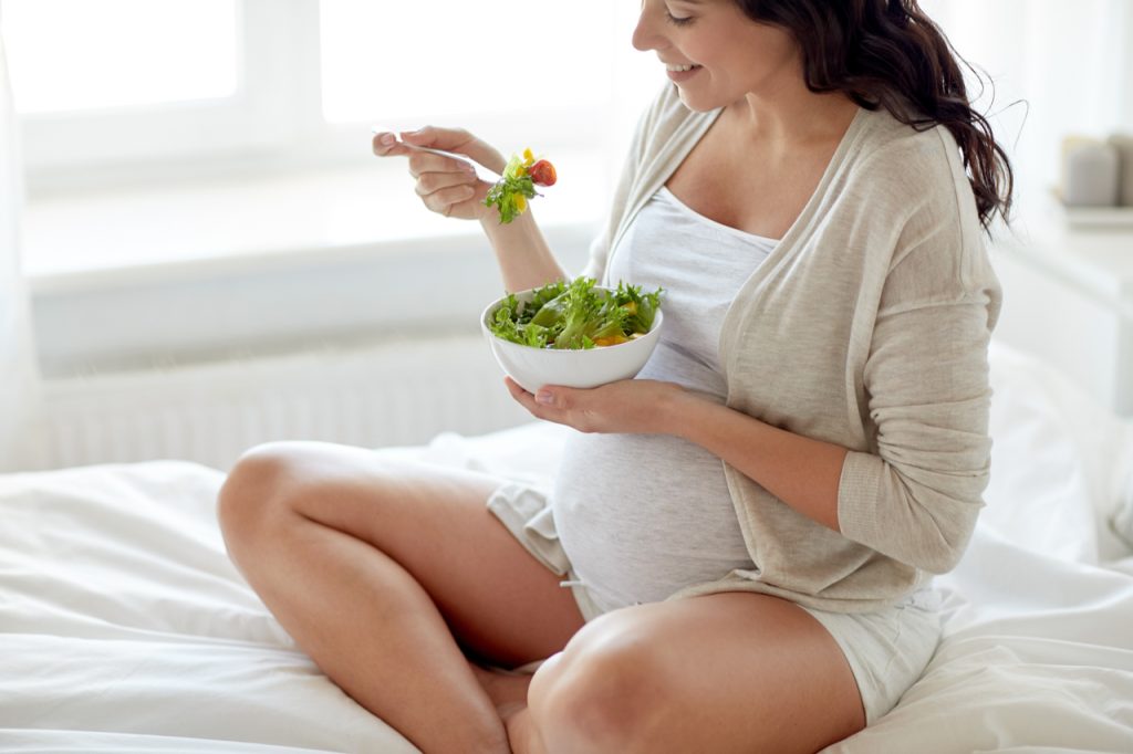 A pregnant woman eating a bowl of salad. Expecting mothers need to take care of themselves starting with what they eat.
