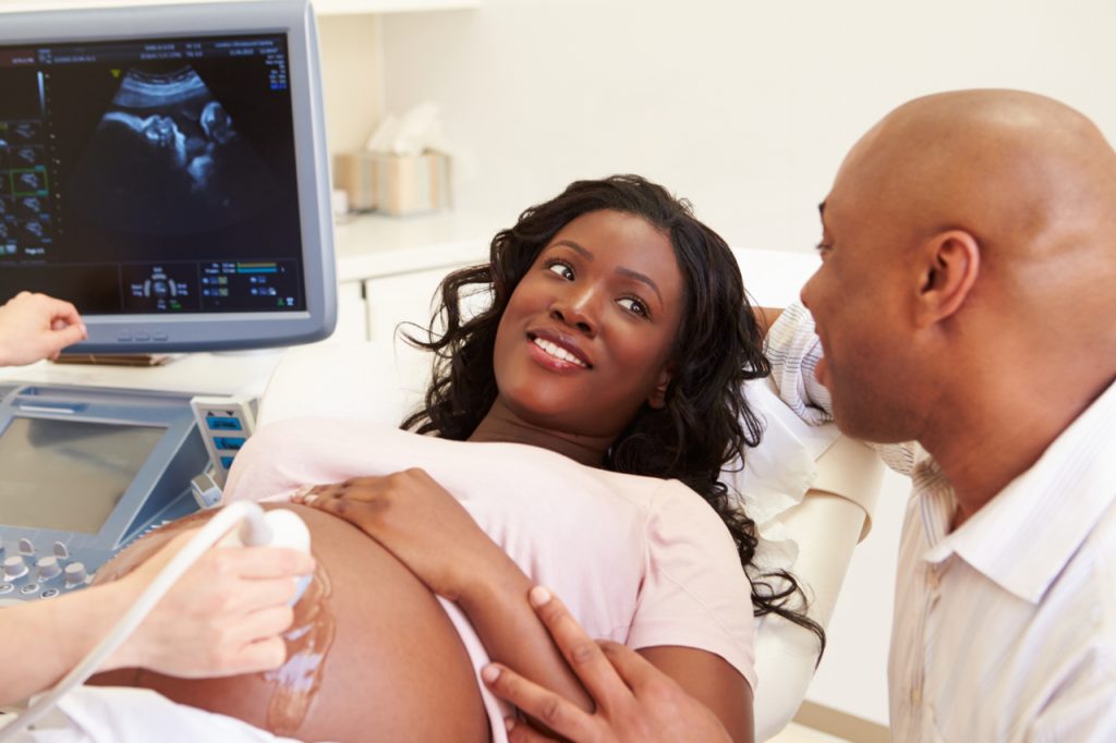A pregnant woman undergoing sonography accompanied by her husband.