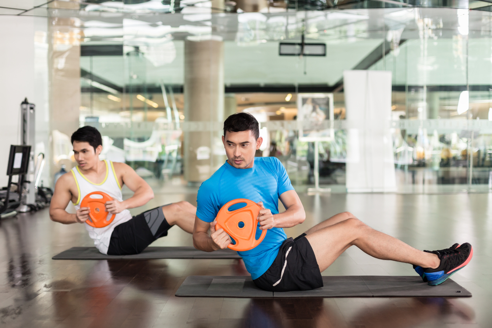 Two men doing weighted twist for the abs.