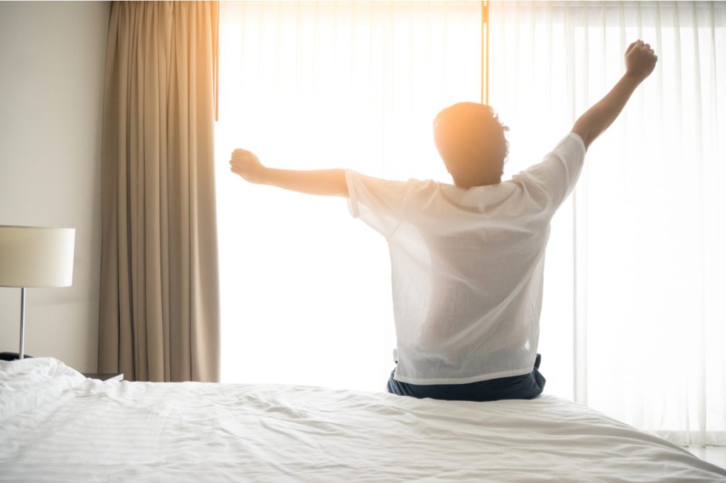 A man raising his hands after waking up early is healthy lifestyle habits.
