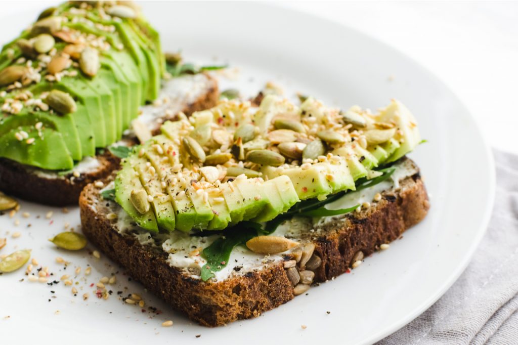 Open face sandwich topped with sliced avocados sprinkled with nuts.