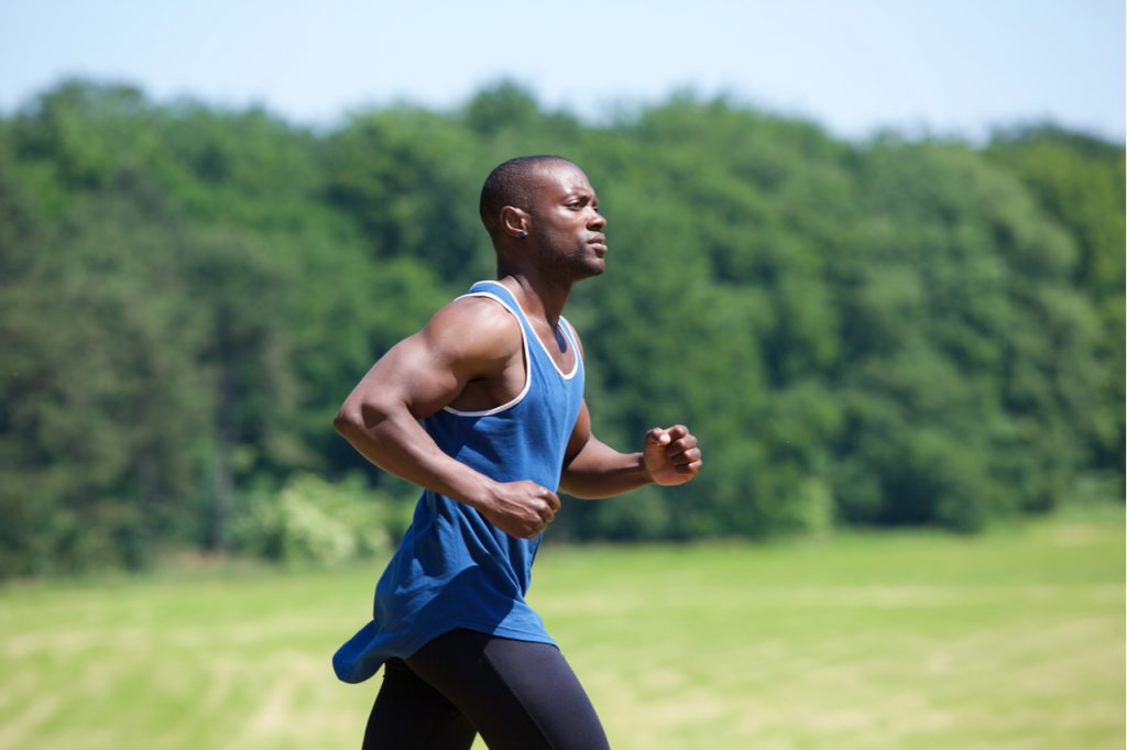 A man running outdoors with natural greenish background.