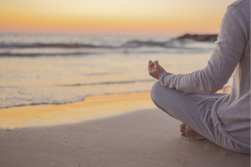 A man practice yoga on the beach at sunset as step to change mindset.