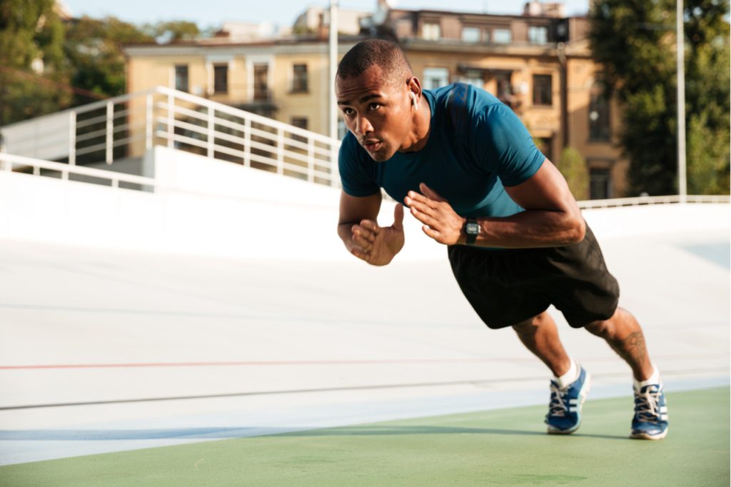 A fit man doing clap push-ups on a track field.