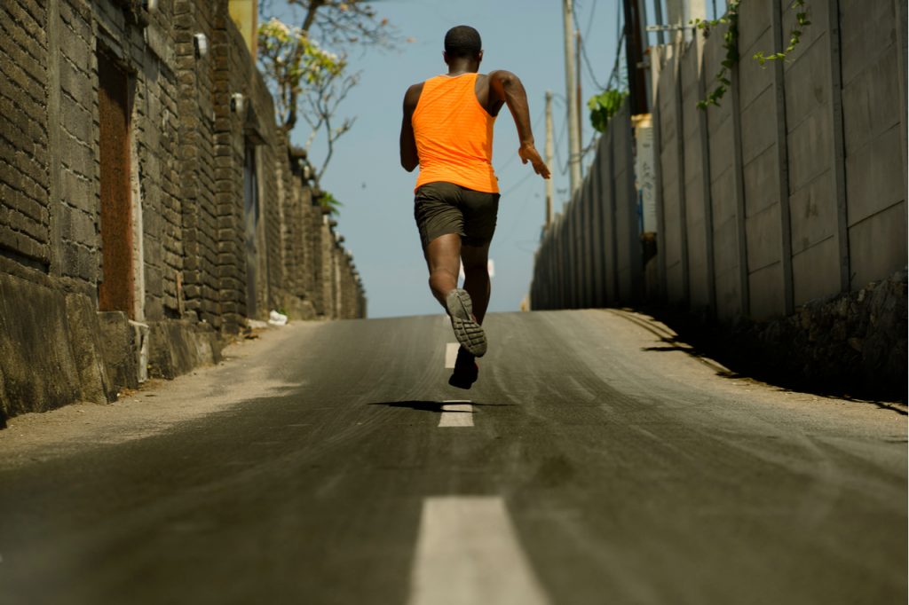 Back view of athletic professional sport man running training hard outdoors on asphalt road.