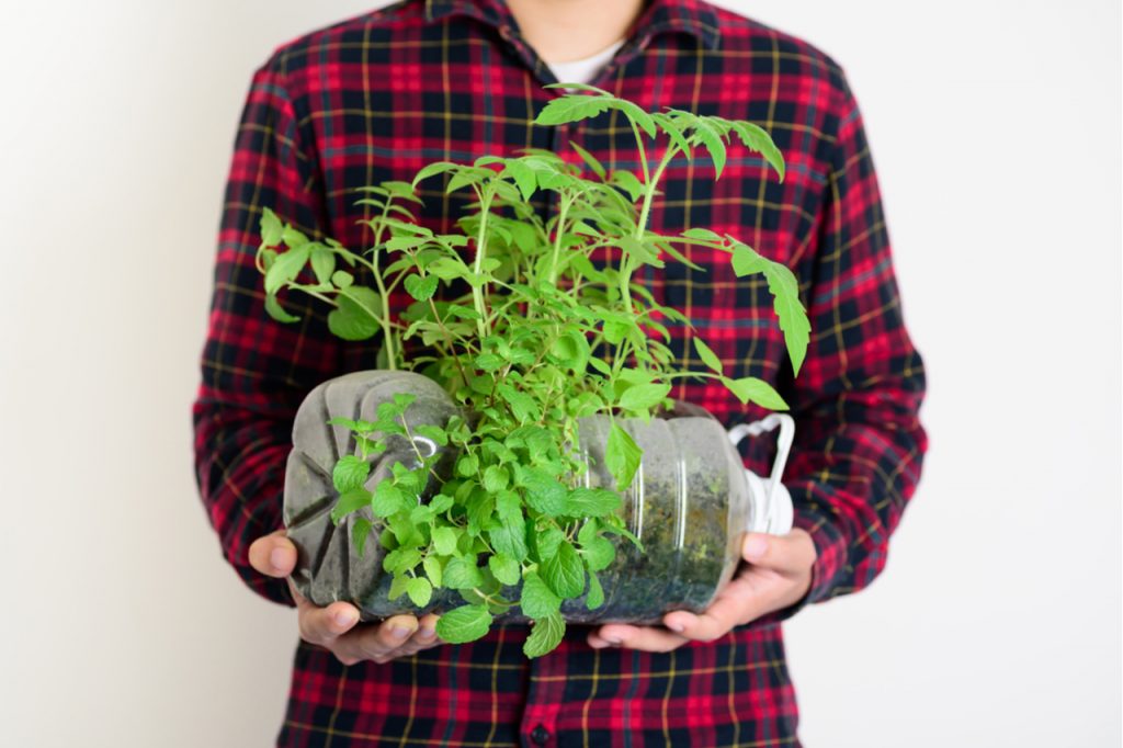 A man holding a plant that uses a recycled water bottle or container.