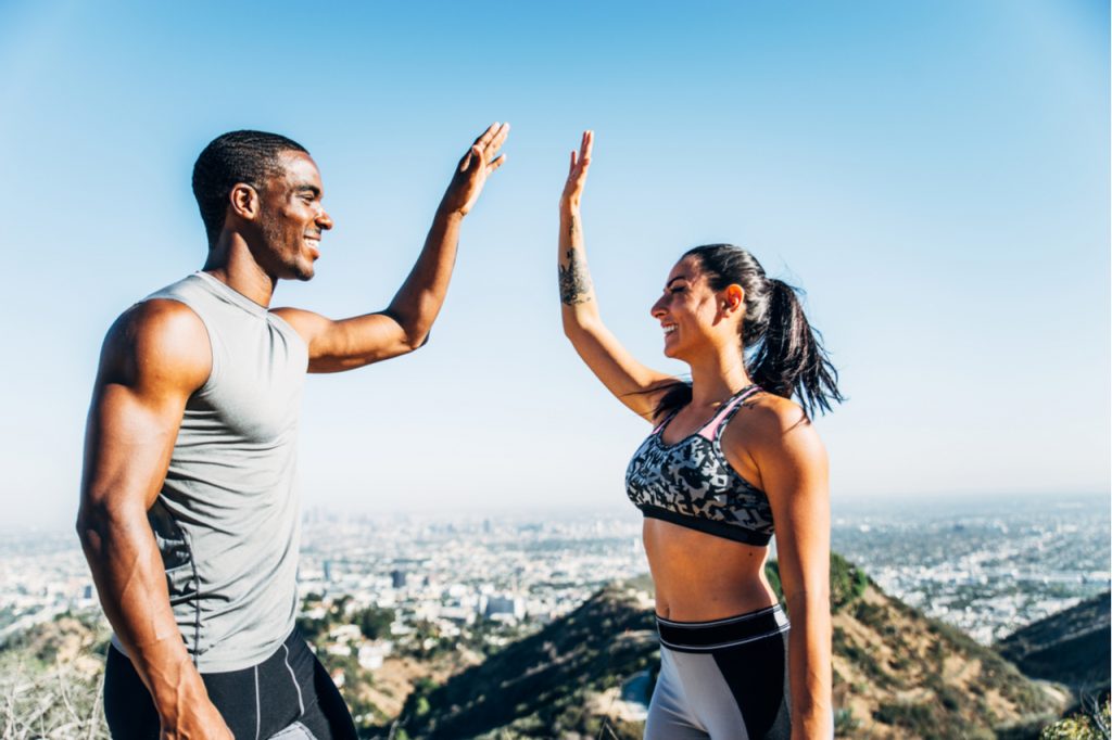 An inter-racial fit couple doing high-five, looks like celebrating a new running record. 