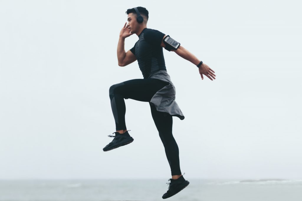Sporty asian man doing jump lunges.