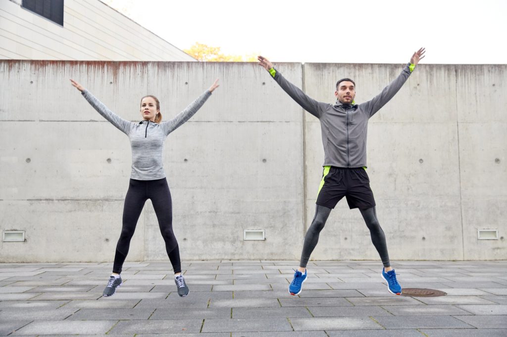 Couple doing jumping jacks to start their full body workout at home.