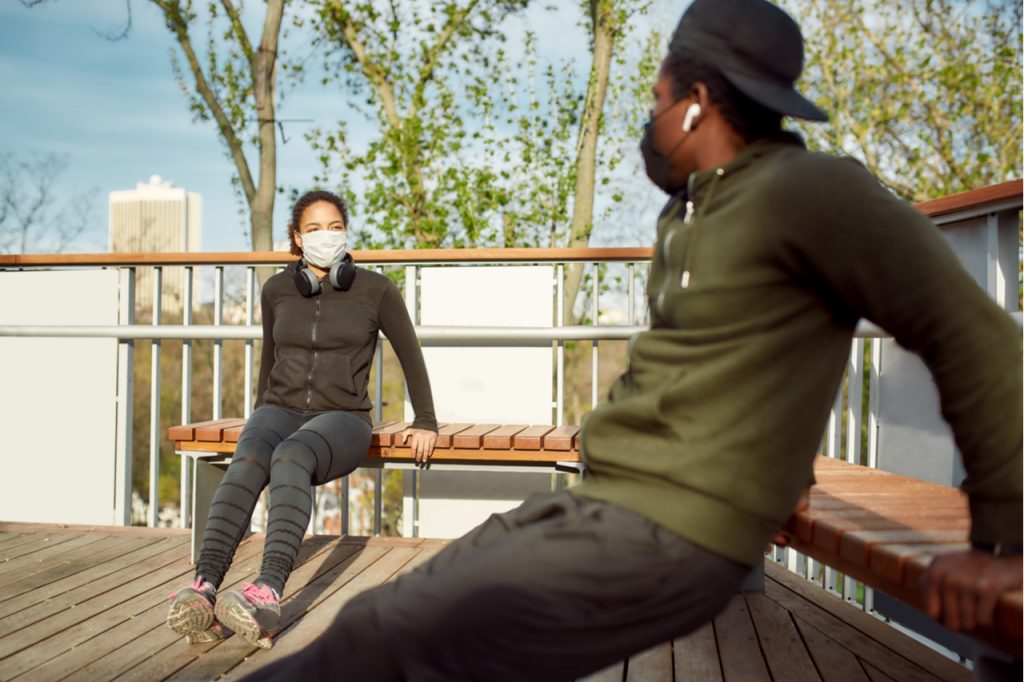 Couple in protective masks doing push-ups exercises on bench.