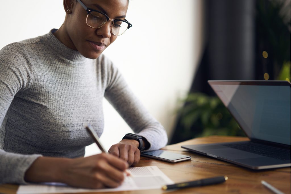Woman reviewing her investments using a laptop, pen and paper.