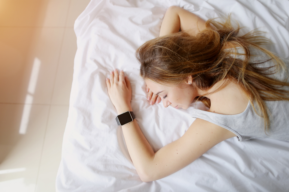 young woman with smartwatches on hand sleep in white bed.