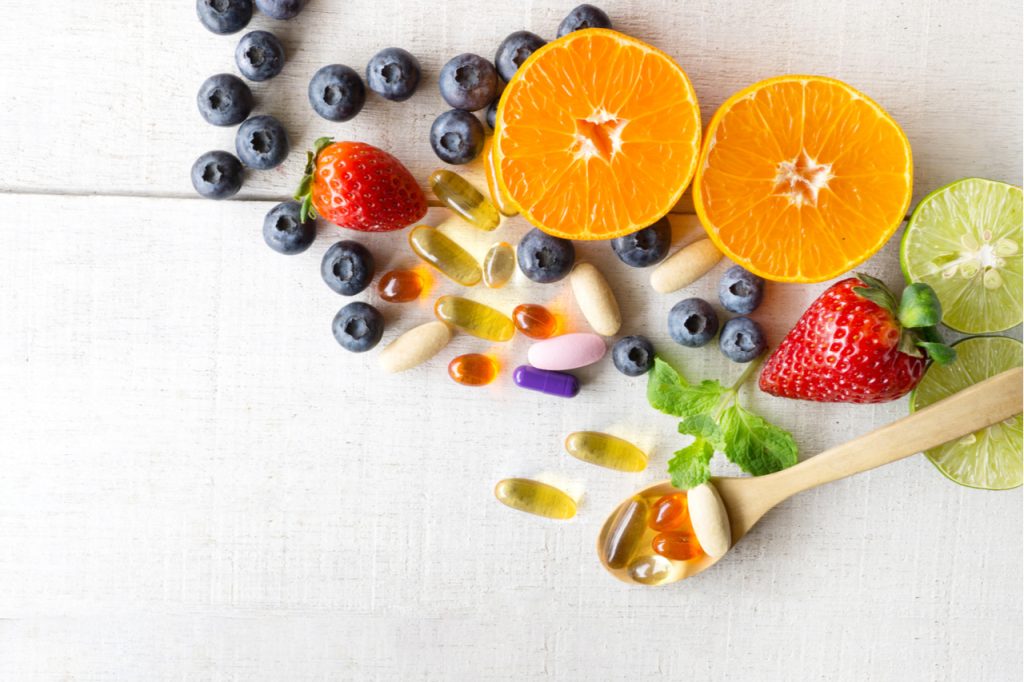Multivitamins and supplements with fresh and healthy fruits on white wooden background as part of beauty tips.