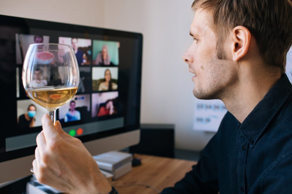 A man holding a wine glass while on a video conference call with his friends.
