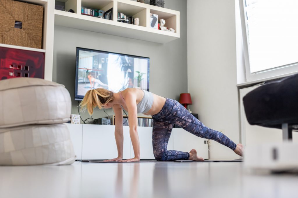 Attractive sporty woman exercising in front of television in her living room.