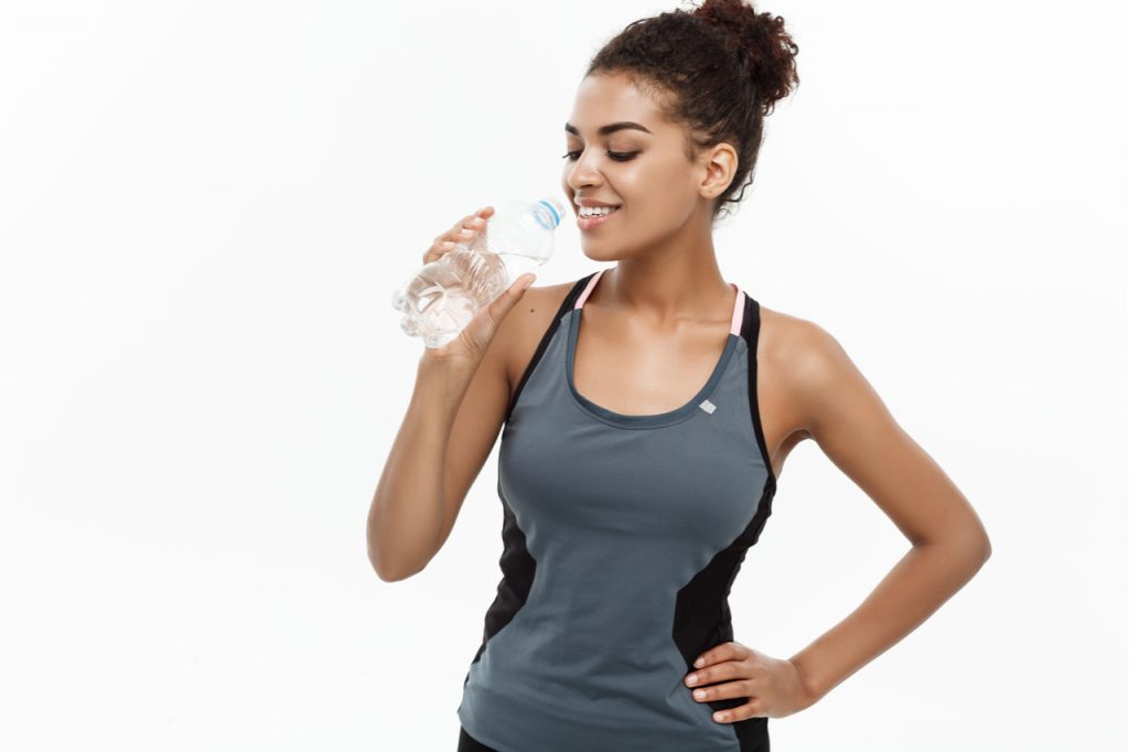 A woman in sport clothes drinking water by plastic bottle after workout.