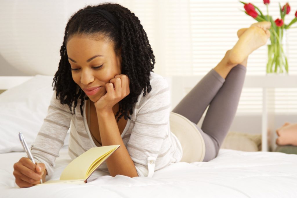 A woman writing on her journal while on bed.
