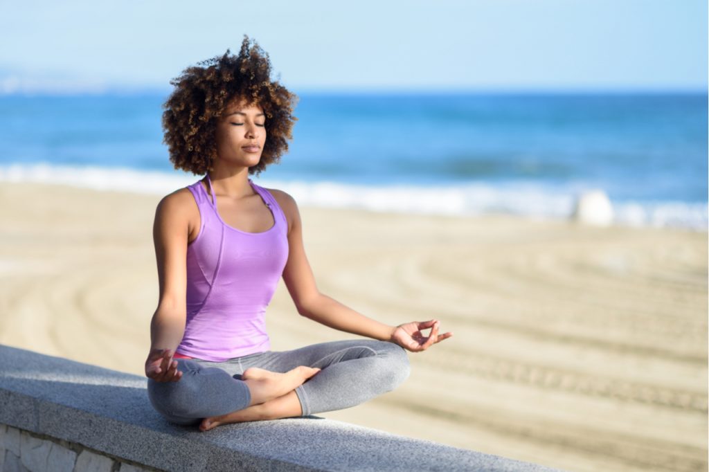 Woman doing yoga asana in the beach with eyes closed