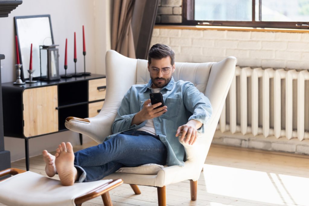 Man sitting comfortably in a chair while using his phone probably browsing the net about sitting the new smoking.