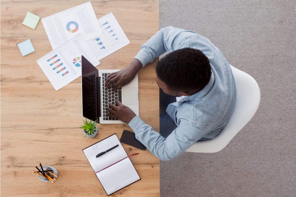 Man working on laptop at wooden desk finding ways to ways to make money from home.